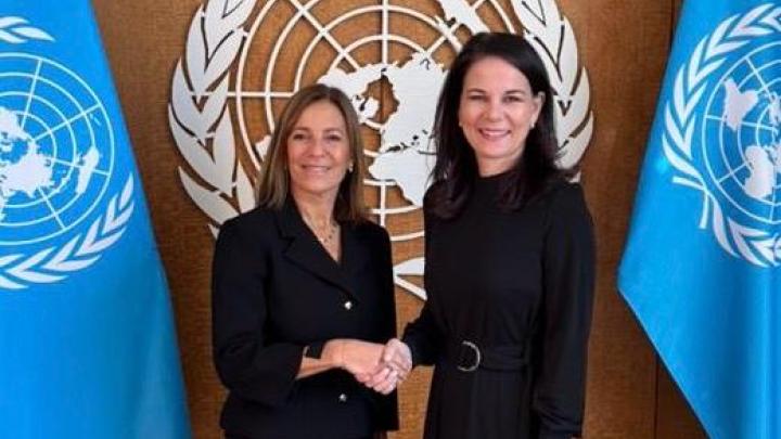 Two women - IRMCT President Gatti Santana and President of the UNGA Ms. Baerbock, shaking hands in front of a UN sign and flags