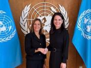 Two women - IRMCT President Gatti Santana and President of the UNGA Ms. Baerbock, shaking hands in front of a UN sign and flags